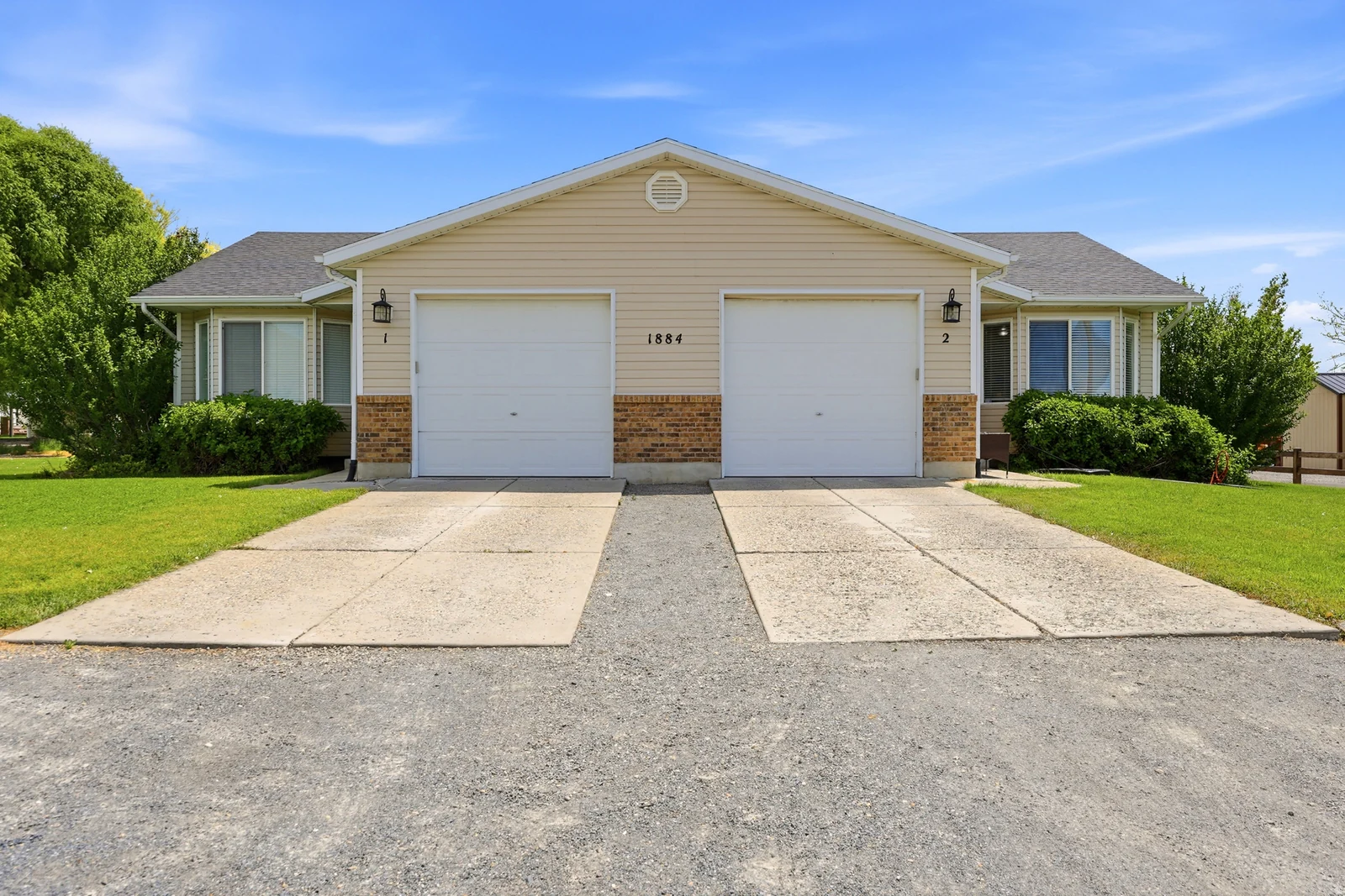 Duplex exterior featuring light-toned siding, brick accents, two single-car garages, and individual concrete driveways